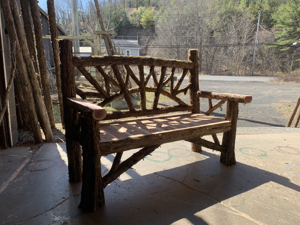 Outdoor park bench built in the rustic style using logs and branches titled the Maverick Bench