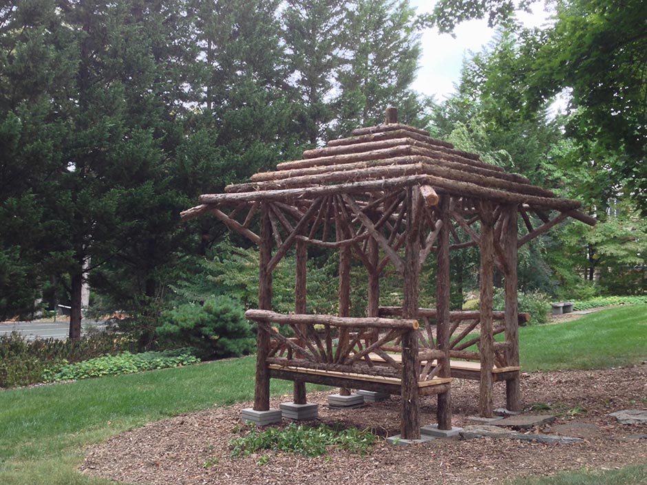 Natural wood sitting shelter built with trees and branches titled the Briarcliffe Shelter