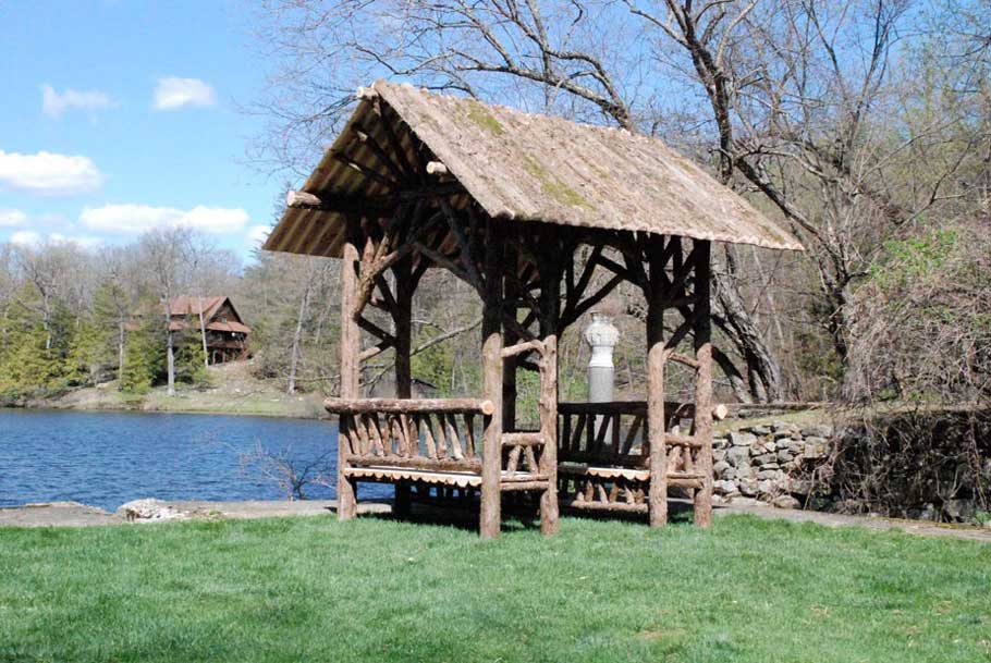 Outdoor rustic covered bench built using bark-on trees and branches titled the Tuxedo Shelter