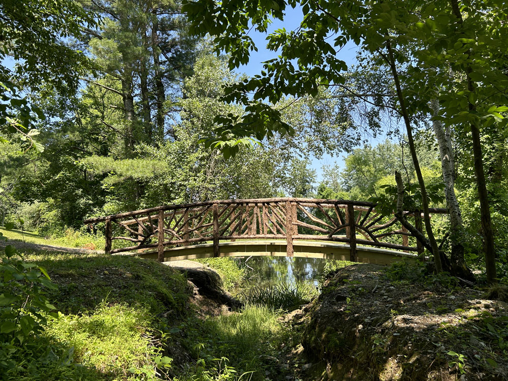 Rustic bridge built using bark-on trees and branches titled the Hillsdale Bridge 