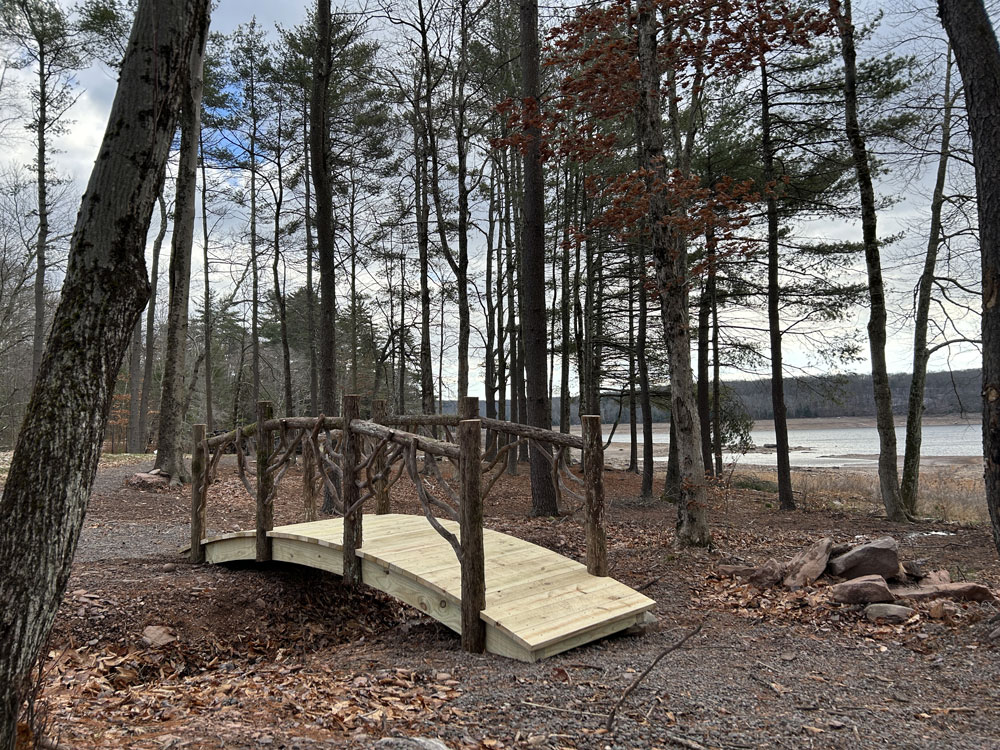 Rustic bridge custom built using cedar trees and branches titled the White Lake Bridge