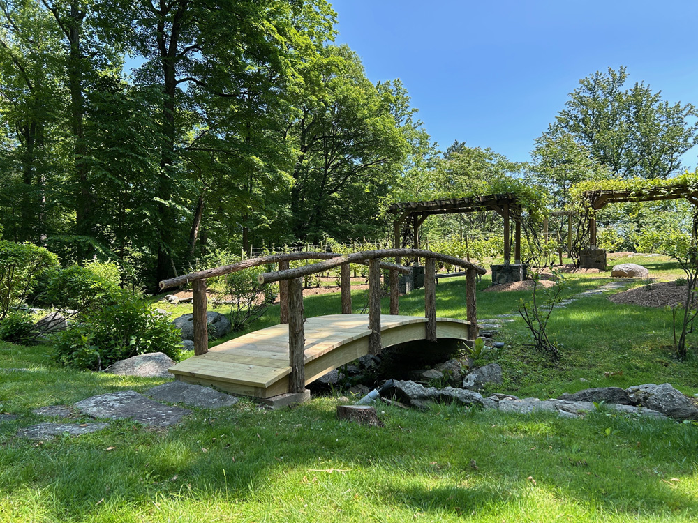Rustic bridge built using bark-on trees and branches titled the Strum Vineyard Bridge