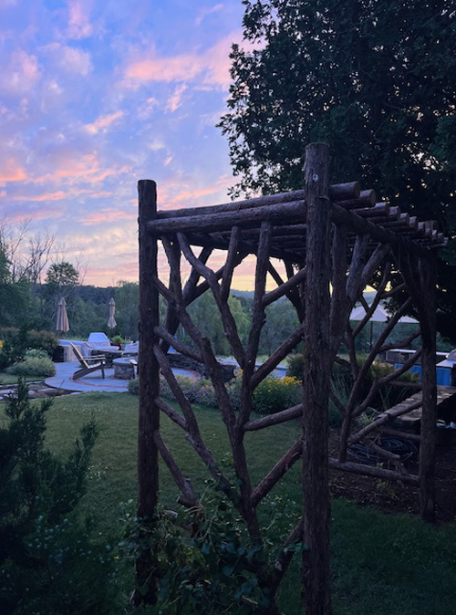 Rustic garden arbor built using bark-on trees and branches titled the Warren Arbor
