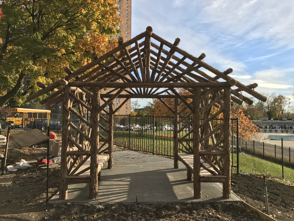 Outdoor rustic sitting shelter built using bark-on trees and branches titled the Skyview Entrance Arbor