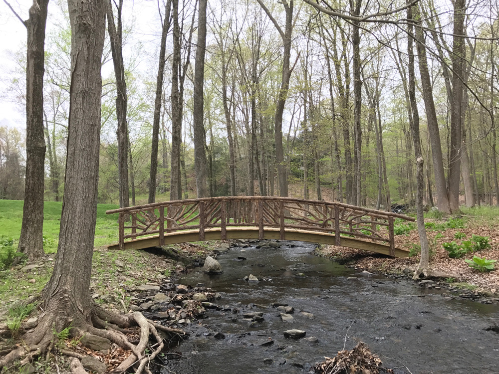 Rustic bridge custom built using cedar trees and branches titled the Storm's Crossing