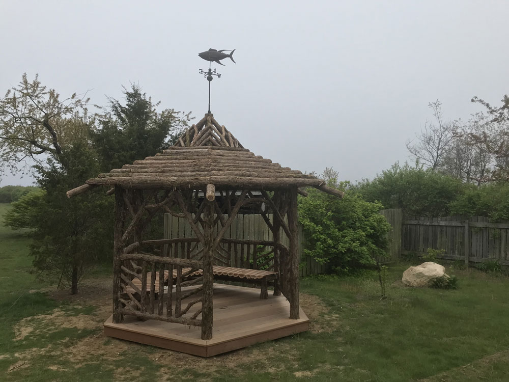 Rustic garden pavilion built using bark-on trees and branches titled the Fishers Island Gazebo