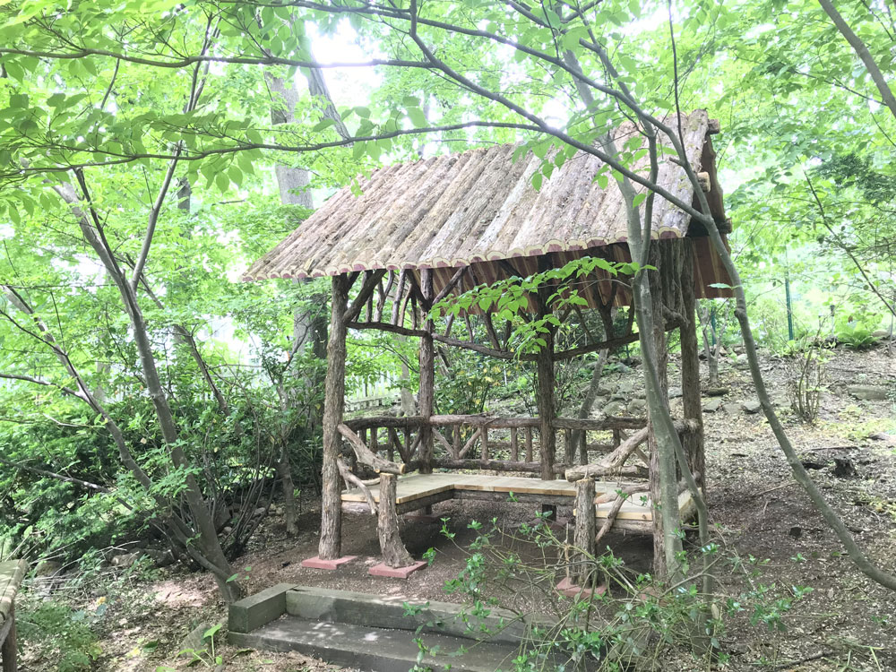 Outdoor sitting shelter built in the rustic style using logs and branches titled the Mayhew Shelter