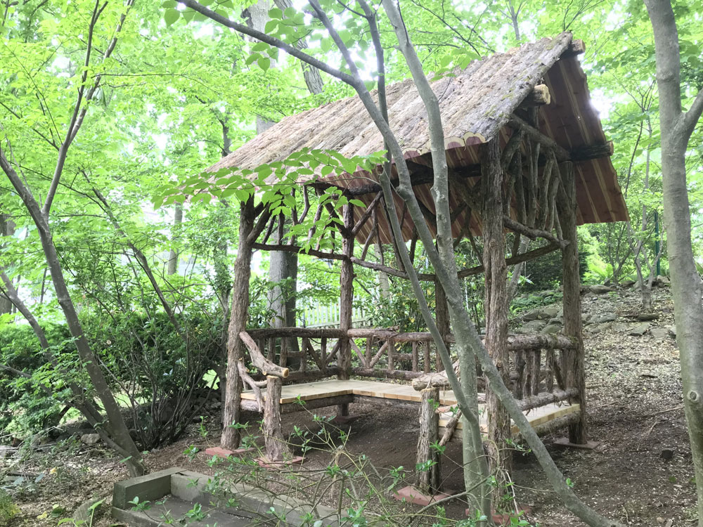 Outdoor rustic sitting shelter built using bark-on trees and branches titled the Mayhew Shelter