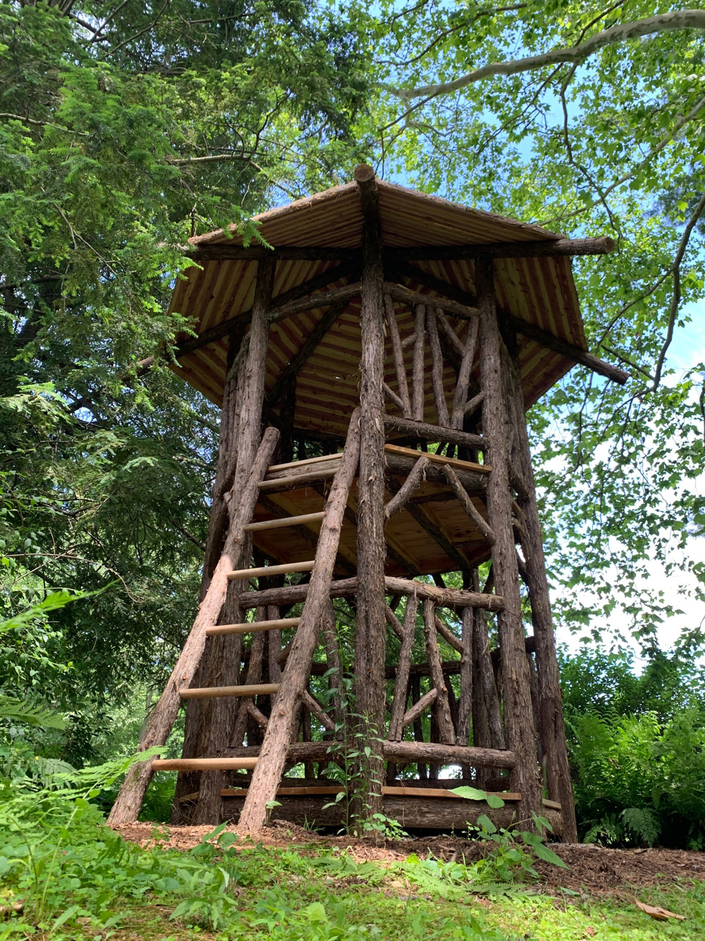 Outdoor rustic play tower built using bark-on trees and branches titled the Bedford Tower