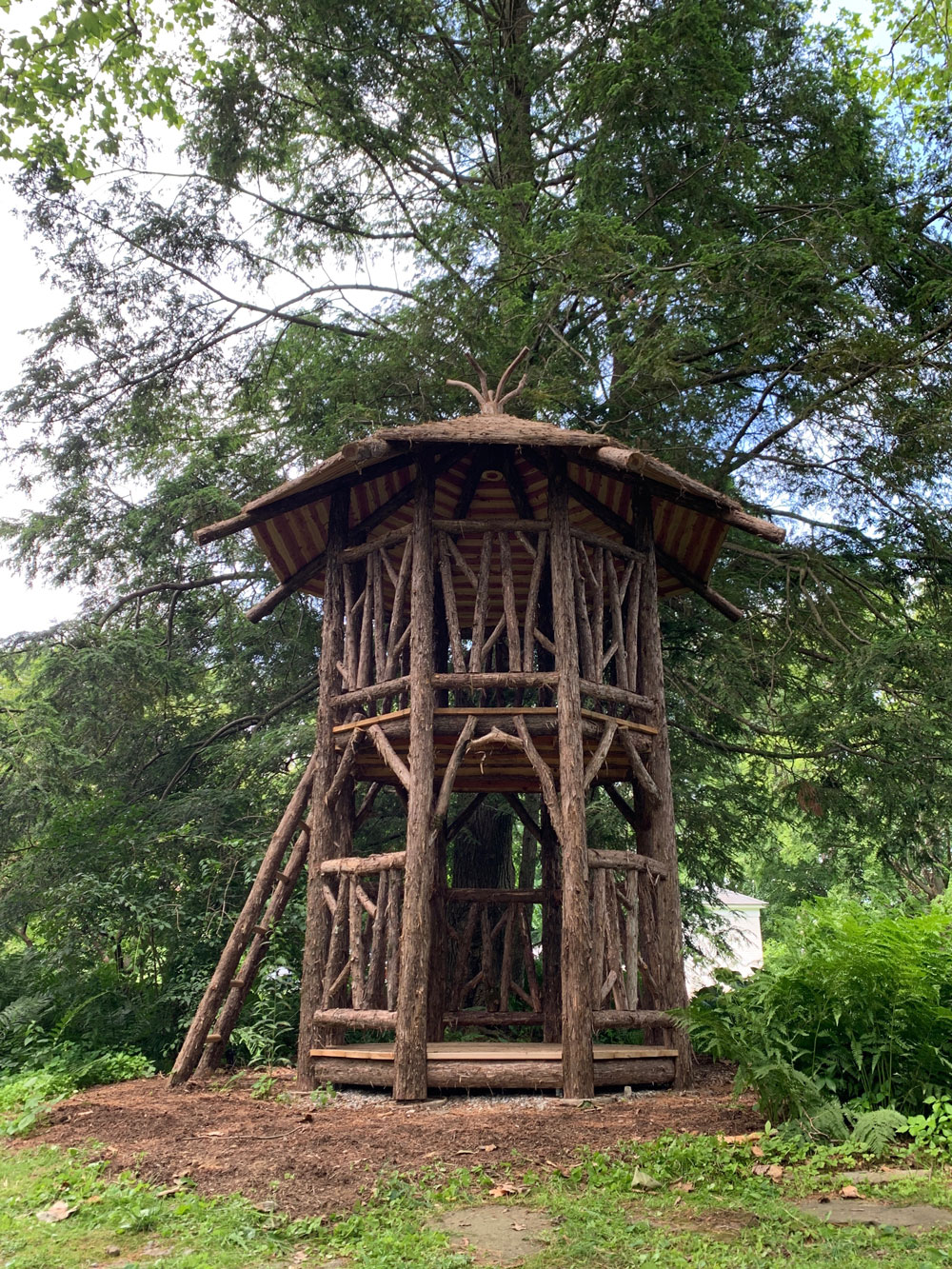 Outdoor rustic play tower built using bark-on trees and branches titled the Bedford Tower