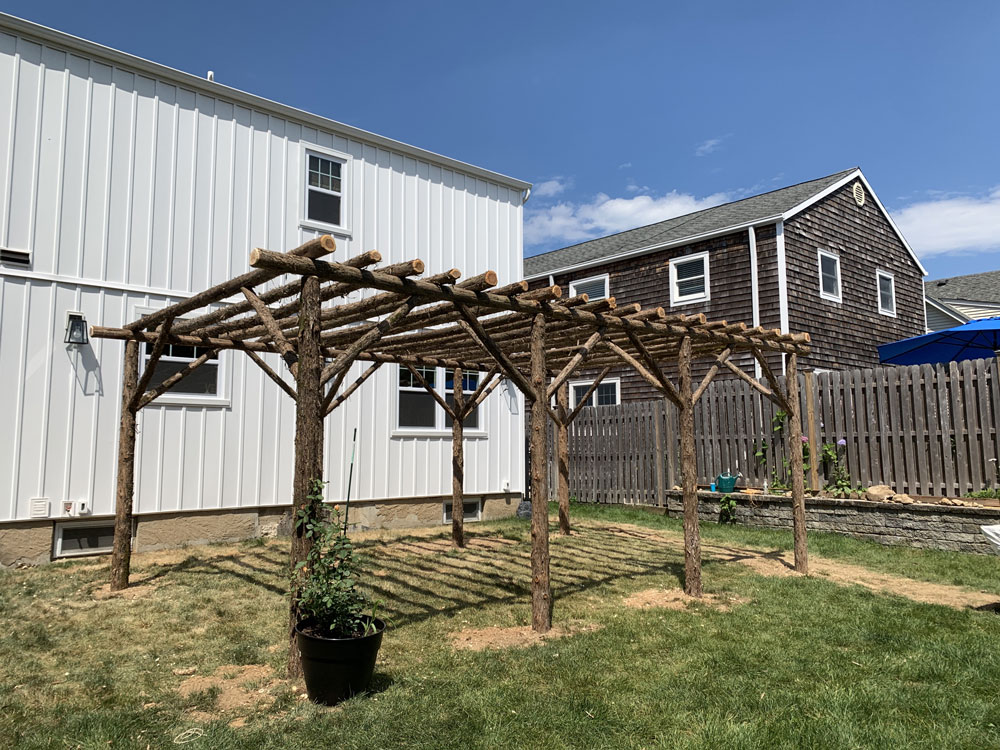 Rustic natural pergola made from bark-on cedar logs, twigs, and branches titled the Northport Pergola