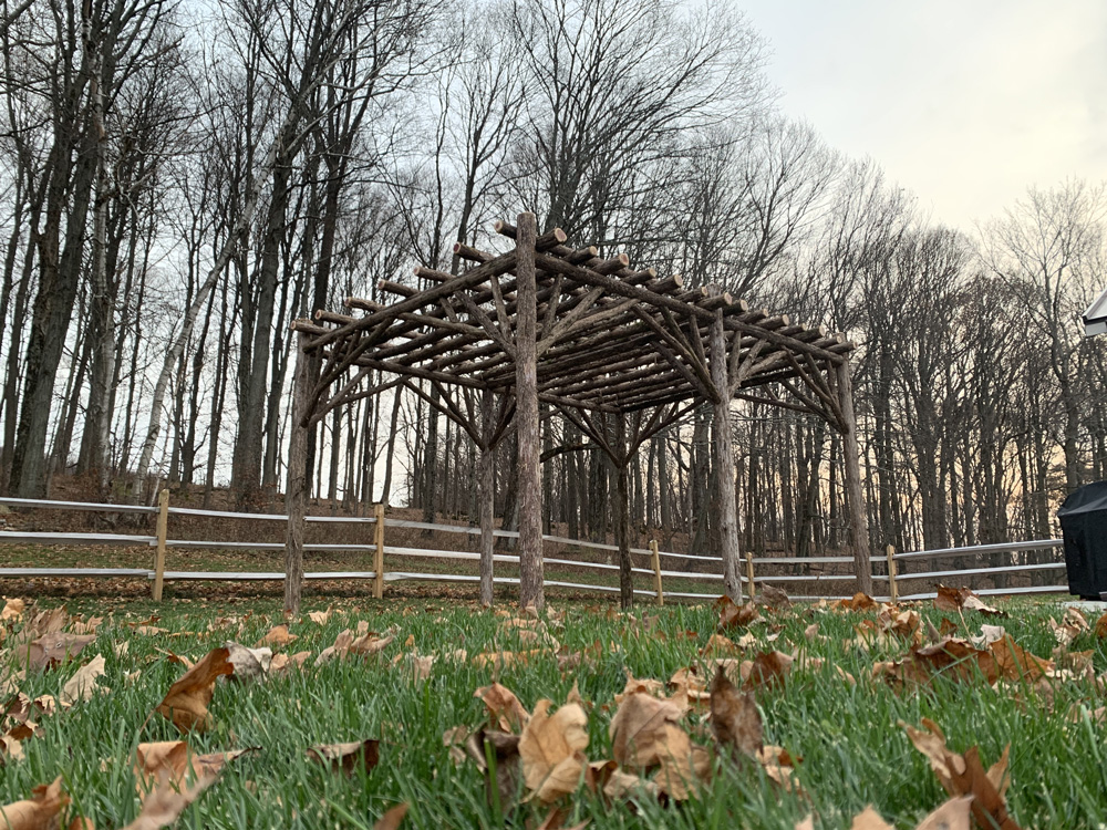 Rustic natural pergola made from bark-on cedar logs, twigs, and branches titled the Pine Plains