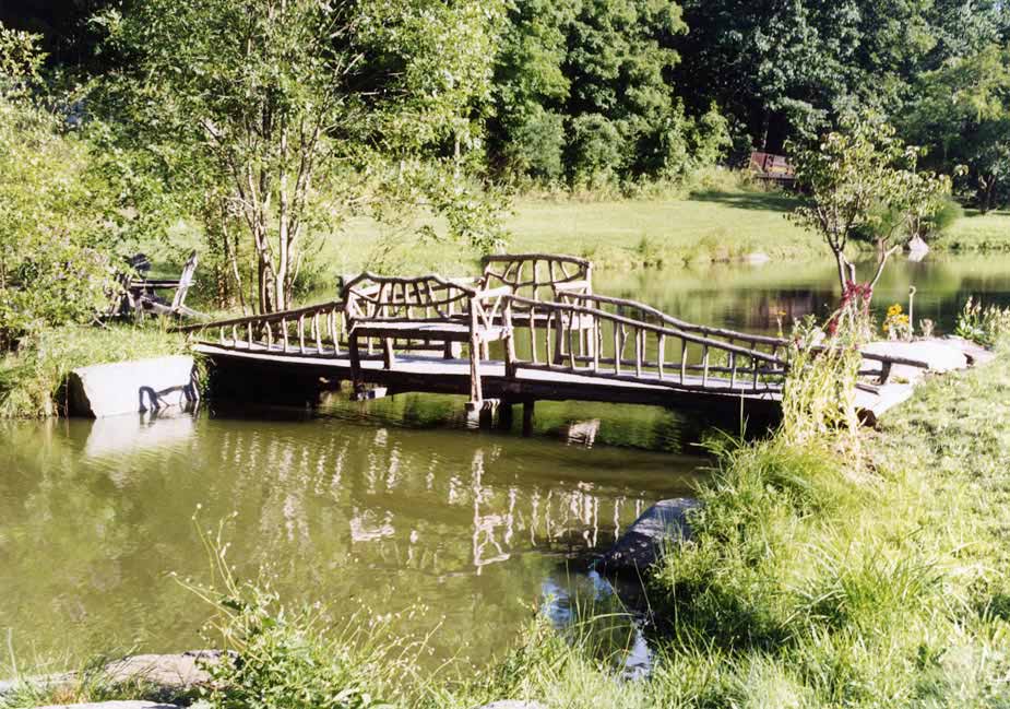 Rustic bridge with benches built using bark-on trees and branches titled the Esopus Bridge