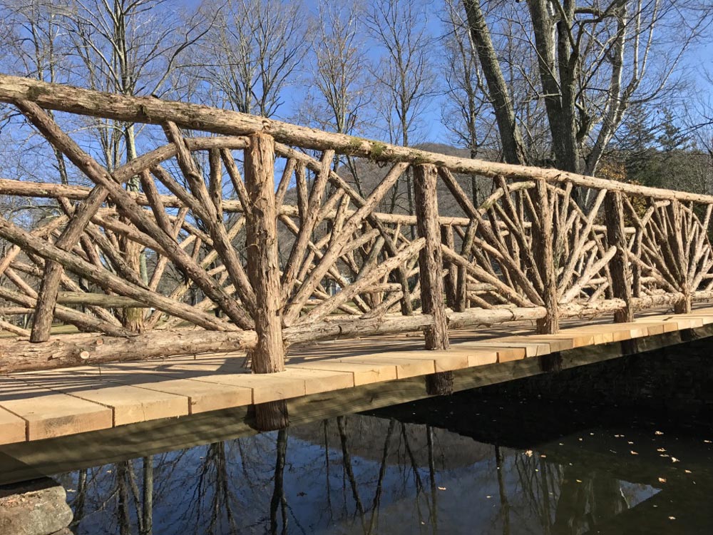 Historic recreation of a rustic bridge crossing a stream built using bark-on trees and branches at Kirkside Park in Roxbury NY