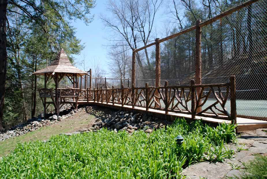 Gazebo and fencing at a personal tennis court built in the rustic style using logs and branches titled the Kamen Summerhouse